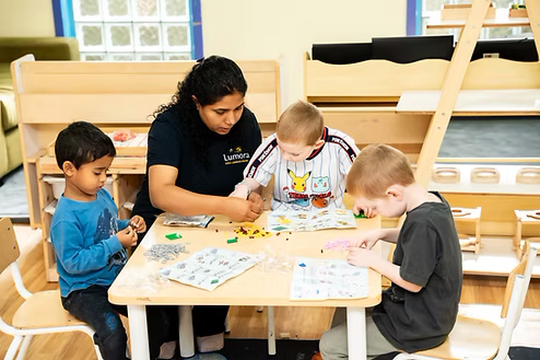 An educator building with blocks at a low table alongside three children