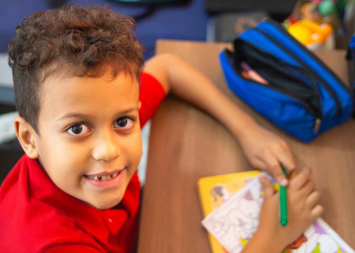 A kinder child drawing at a table with their pencil case nearby